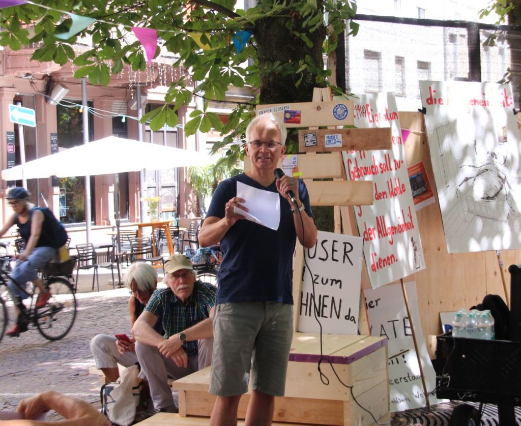 Matthias Lohrer hält eine Rede. Im Hintergrund sieht man Zuhörer, eine Radfahrerin und Plakate von der Kundgebung.