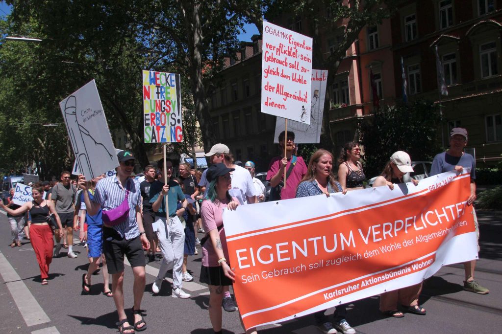 Ein Demonstrationszug. Die Teilnehmer tragen Transparente mit den Aufschriften "Eigentum verpflichtet. Sein Gebrauch soll zugleich dem Wohle der Allgemeinheit dienen." und "Zweckentfremdungsverbotssatzung".